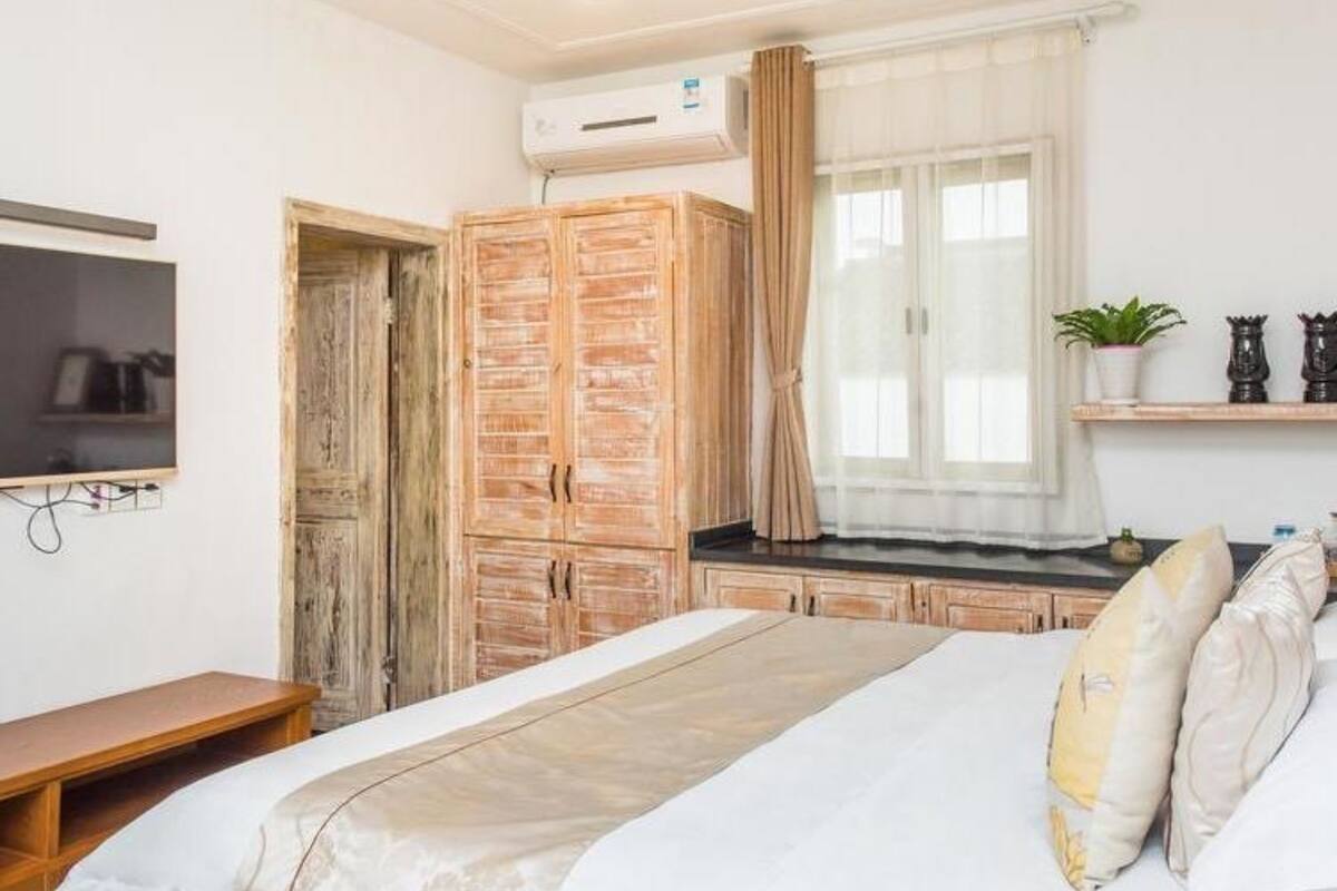 Een slaapkamer met een bed, een houten garderobe, een aan de muur bevestigde televisie en een raam met gordijnen.