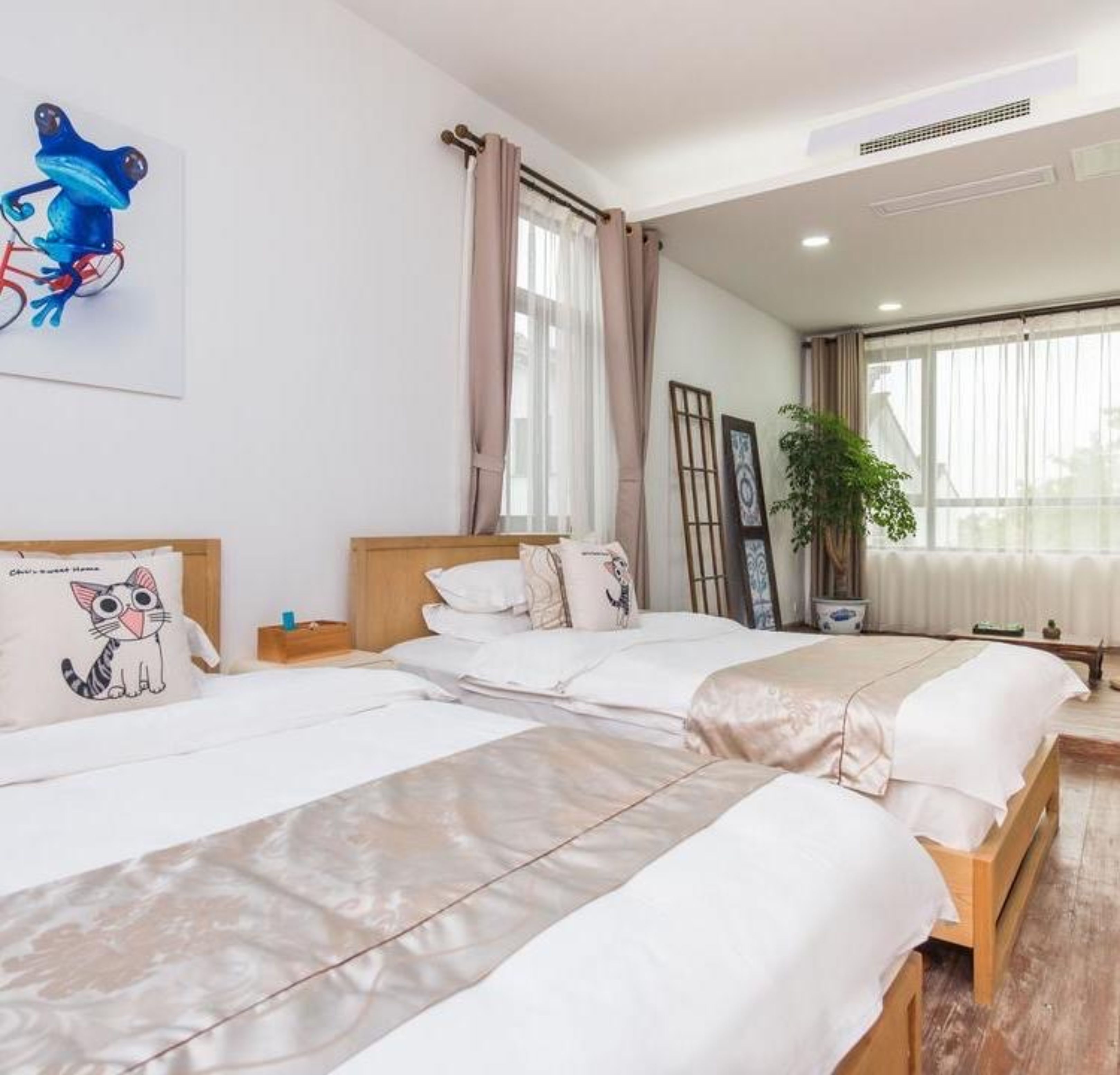 A hotel room with two beds, a large window with curtains, a wall-mounted artwork of a frog, and a potted plant.
