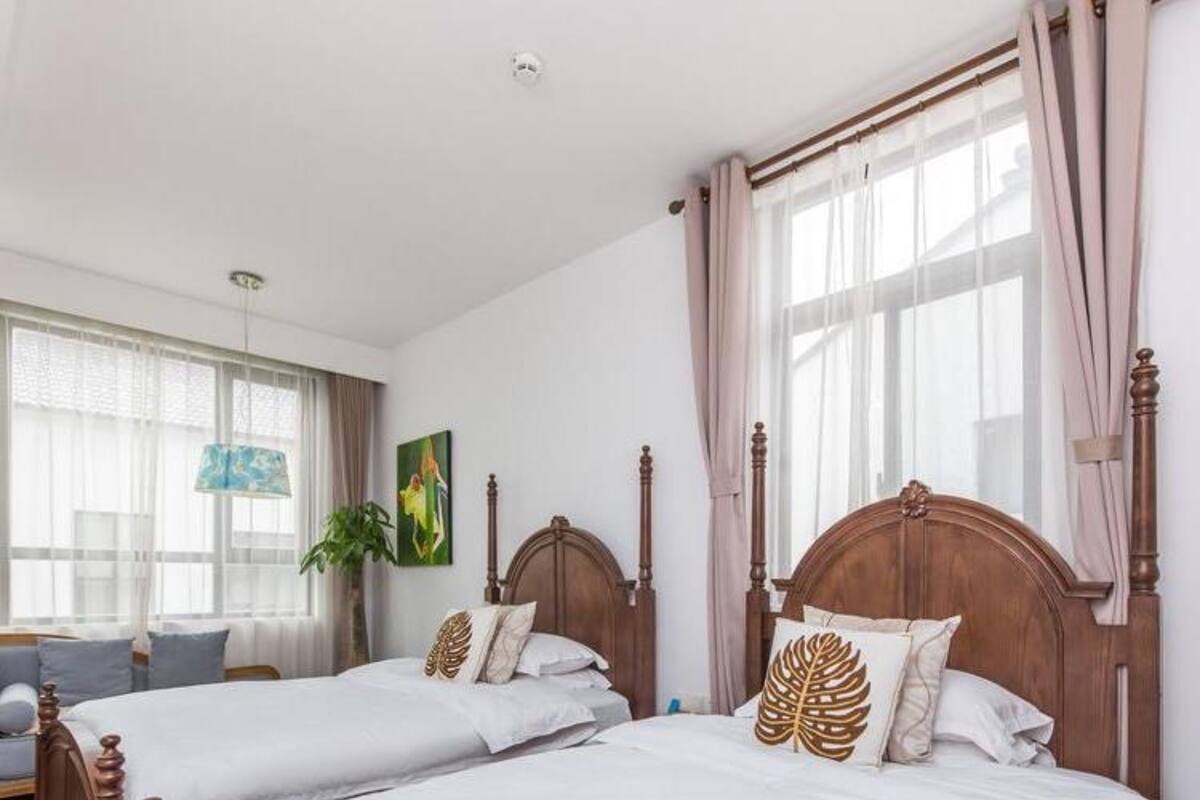 Een hotelkamer met twee houten bedden, wit beddengoed en een groot raam met dunne gordijnen.