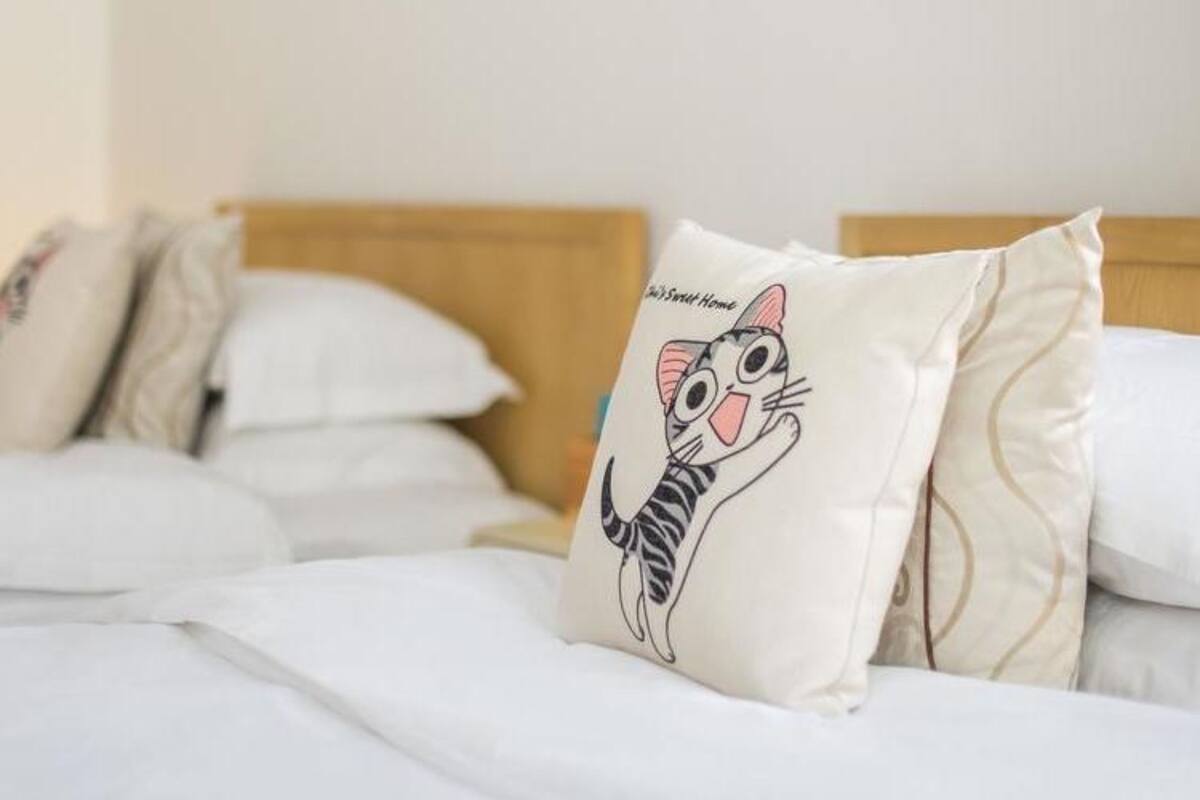Een bed met witte lakens en een kussen waarop een cartoonkat staat.