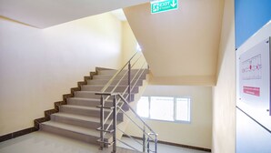 A staircase with a metal railing, a sign indicating an exit, and a window on the right wall. - Wises Hotel (Chachoengsao)