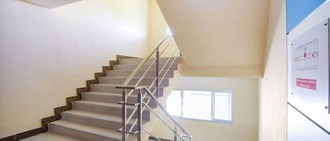 Un escalier avec une rampe en métal, un panneau indiquant une sortie et une fenêtre sur le mur de droite.