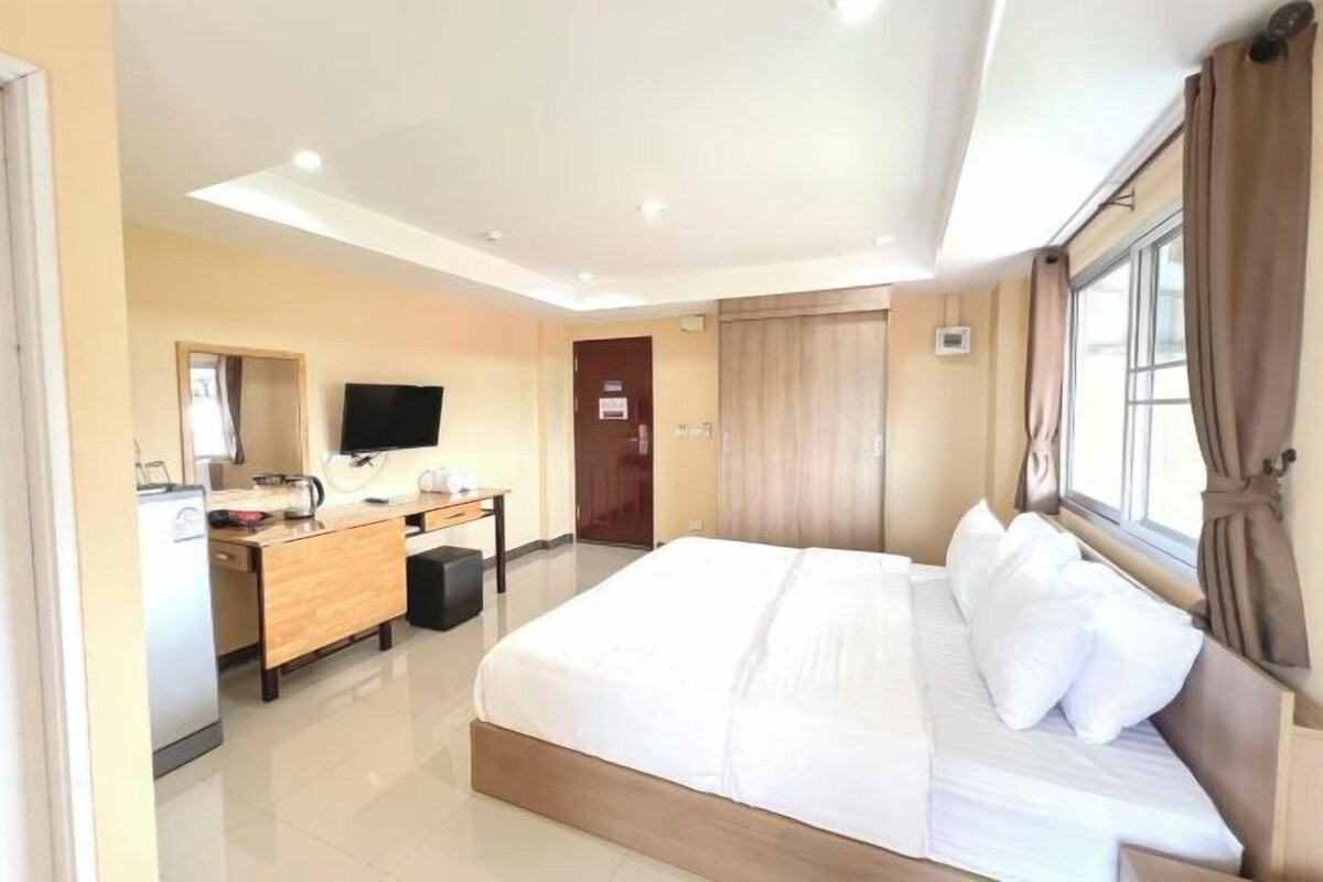 Una habitación de hotel con una cama grande, un escritorio con computadora, televisión y una ventana con cortinas.