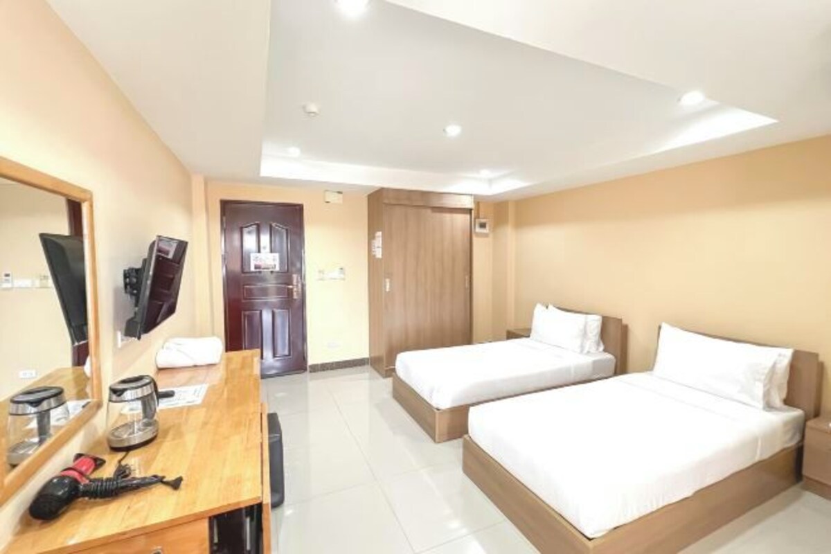 Una habitación de hotel con dos camas individuales, un escritorio de madera con un ordenador y una cafetera, un espejo y un armario.