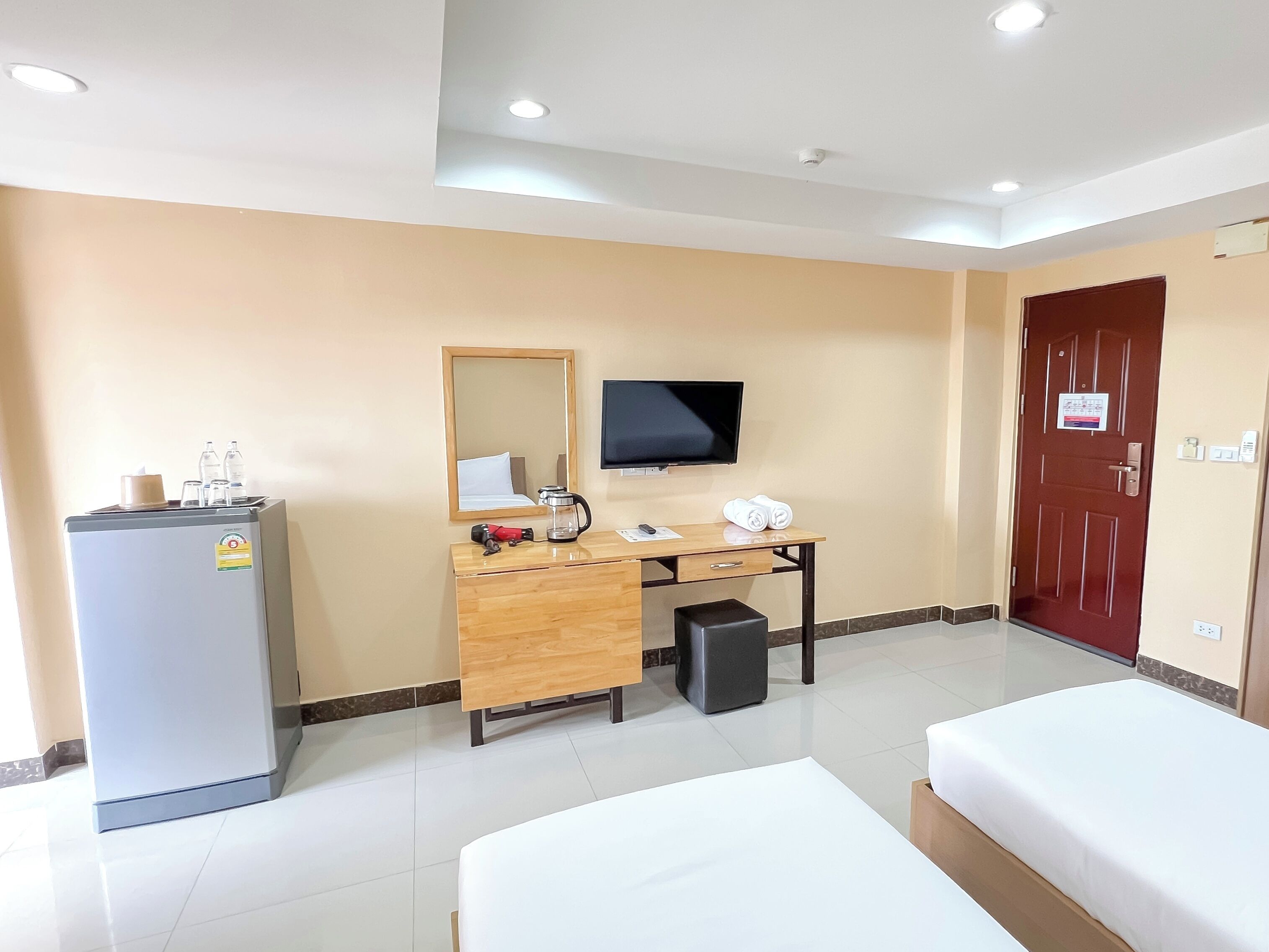 Habitación de hotel con cama, escritorio con computadora, televisor y un minibar, y una puerta roja.