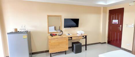 Habitación de hotel con cama, escritorio con computadora, televisor y un minibar, y una puerta roja.