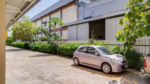 A parking area with a car, a building with a metal roof, and some greenery. - Wises Hotel (Chachoengsao)