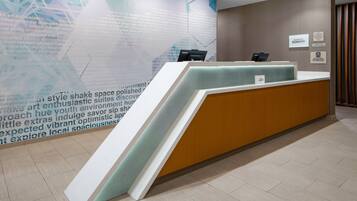 A hotel reception desk with a modern design, a large informational wall, and a clean, tiled floor.