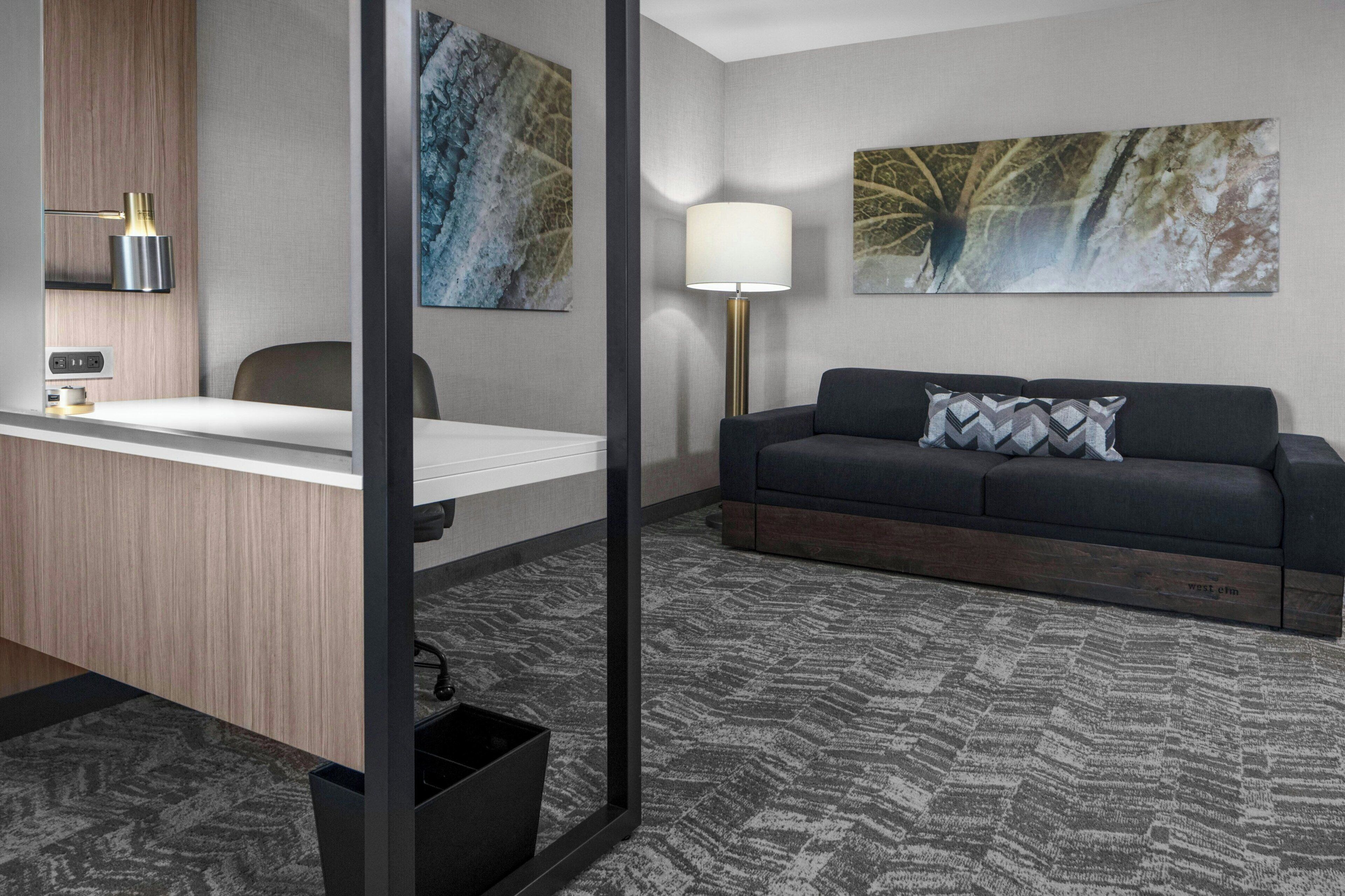 Een moderne hotelkamer met een bureau, een bank en twee grote abstracte schilderijen aan de muur.