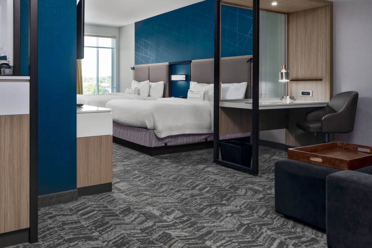 A modern hotel room with a large bed, a desk, a chair, and a view of the outdoors.