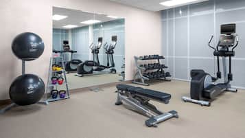 A gym with exercise equipment, a mirrored wall, and a weight rack.