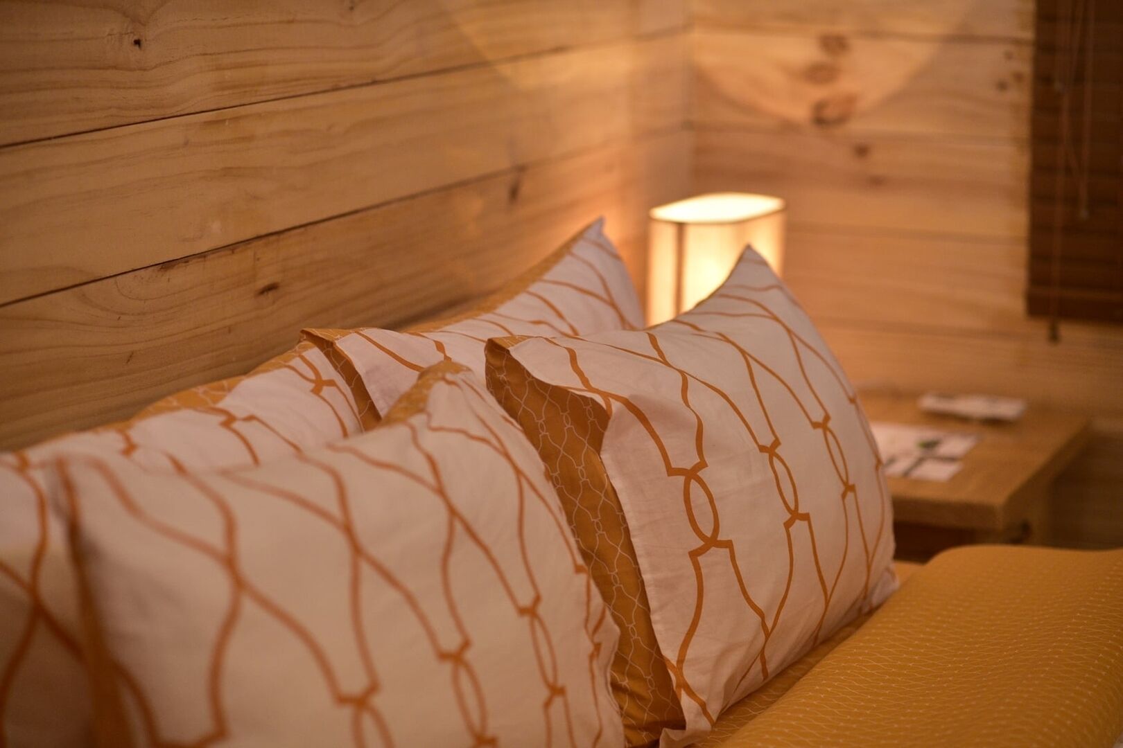 A wooden cabin interior with a bed featuring patterned pillows and a yellow blanket.