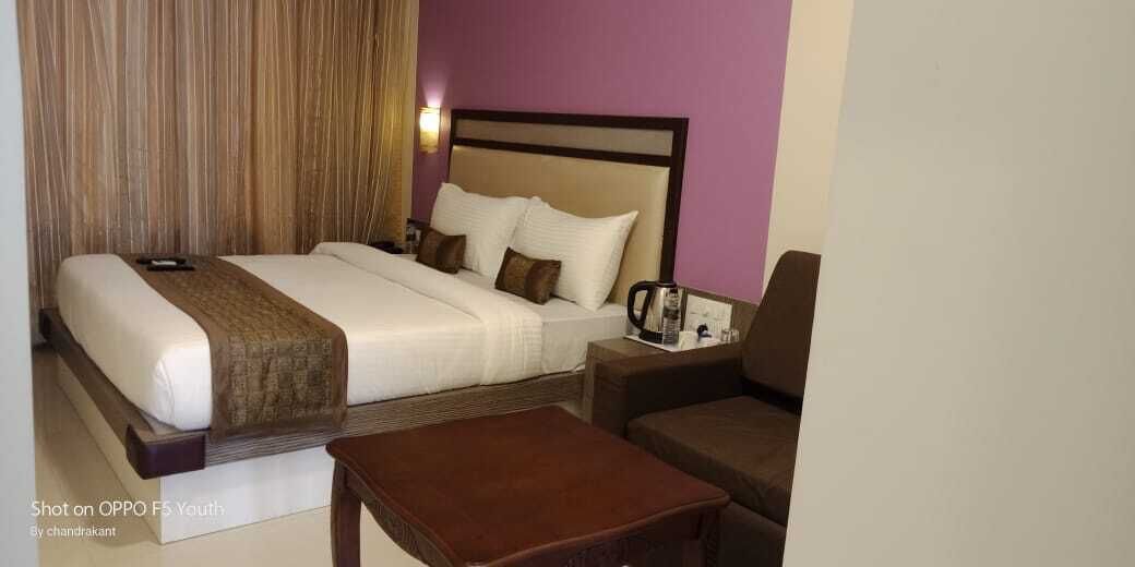 A hotel room with a bed, a nightstand, a coffee maker, and a seating area.