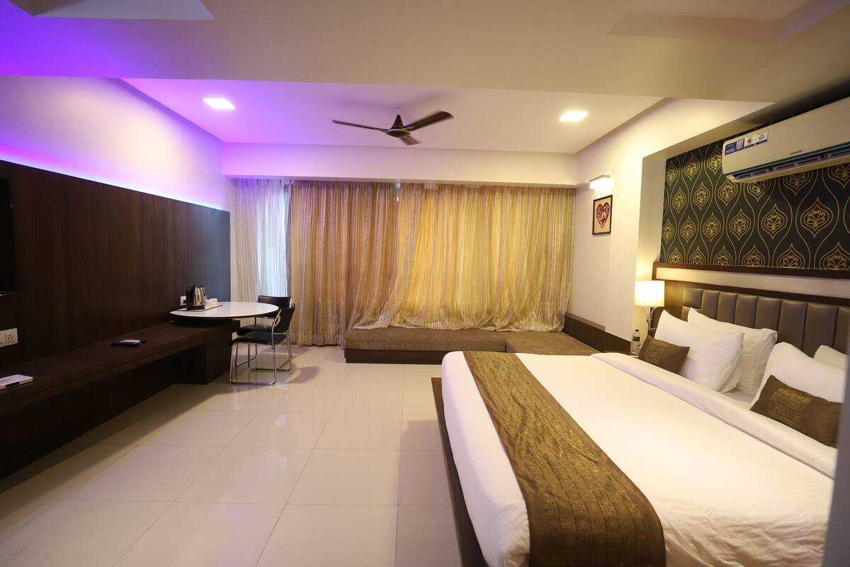 A hotel room with a bed, a desk, a chair, a ceiling fan, and a large window with curtains.