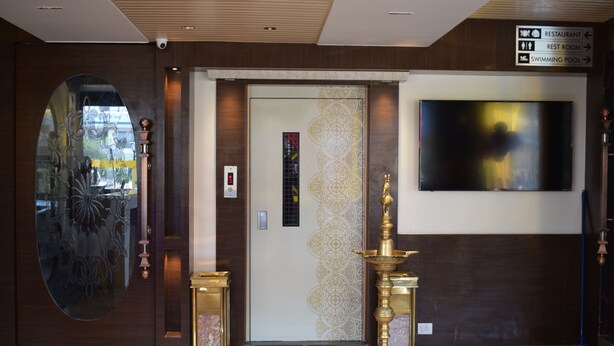Vestíbulo de hotel con mostrador de recepción, pared decorativa con televisor y señalización que indica servicios como restaurante, baños y piscina.