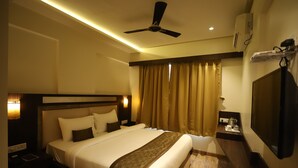 Habitación de hotel con una cama grande, ventilador de techo, televisión y mesita de noche con lámpara.