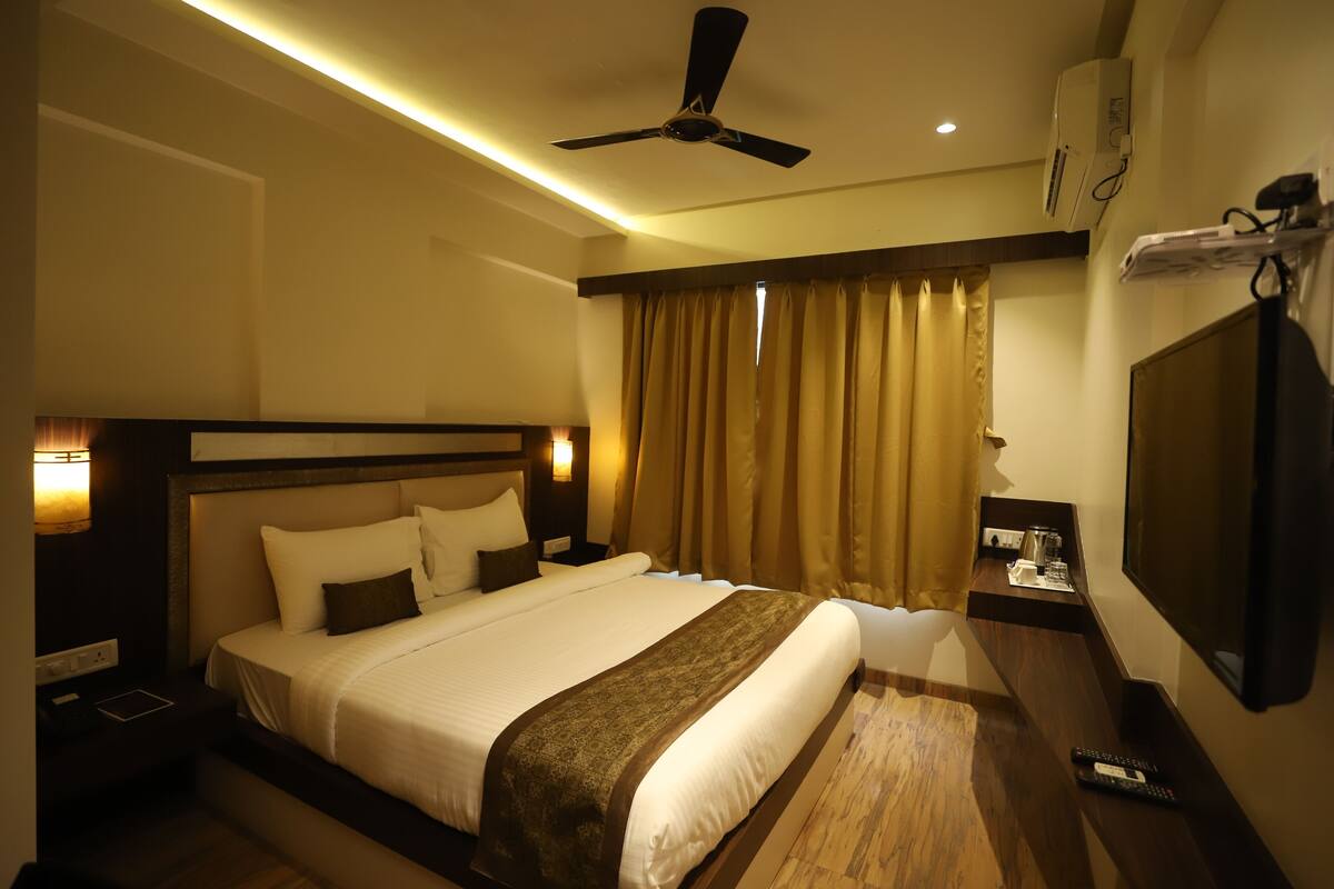 A hotel room with a large bed, a ceiling fan, a TV, and a bedside table with a lamp.