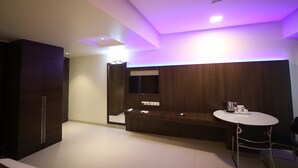 Una habitación de hotel moderna con un tocador de madera, una mesa redonda con una silla y un televisor de pantalla plana montado en la pared.