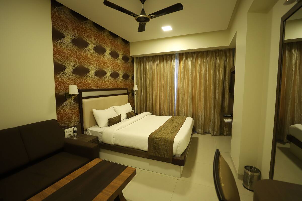 A hotel room with a bed, a sofa, a desk, a ceiling fan, and a curtain.