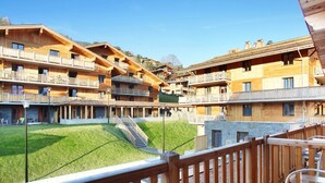 A wooden chalet-style building with multiple balconies, a central courtyard with a staircase, and a clear view of the surrounding landscape.