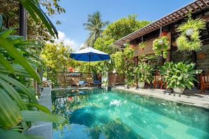 A swimming pool surrounded by lush greenery and potted plants. - Sands River Hoi An Villa (Da Nang)