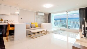 Un salon moderne avec un canapé, une table basse et une vue sur l’océan grâce à de grandes portes coulissantes.