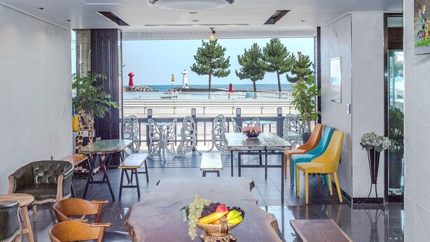 Un intérieur moderne avec vue sur la mer, comprenant un coin repas avec un panier de fruits, différentes chaises et une table.