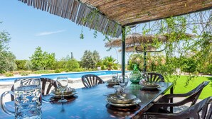 Un espace extérieur aménagé pour prendre les repas, avec une piscine en arrière-plan.