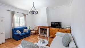 Un salon avec un canapé bleu, un canapé blanc, un meuble en bois sur lequel se trouve un téléviseur, et une cheminée.