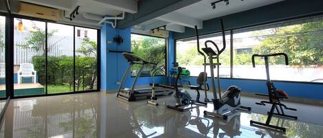 Un gimnasio con equipo de ejercicio, ventanas amplias y vistas a zonas verdes.