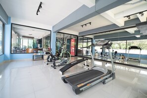 Un gimnasio con cintas de correr, bicicletas estáticas y un espejo grande.