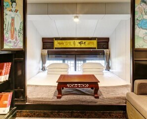 A traditional room with a bed, pillows, a wooden table, and framed artwork. - Floral Hotel Sui Yuan Pingyao (Jinzhong)
