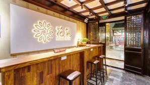 A reception desk with a floral logo and the name "Floral Hotel" above it. There are two bar stools and a potted plant on the counter. - Floral Hotel Sui Yuan Pingyao (Jinzhong)