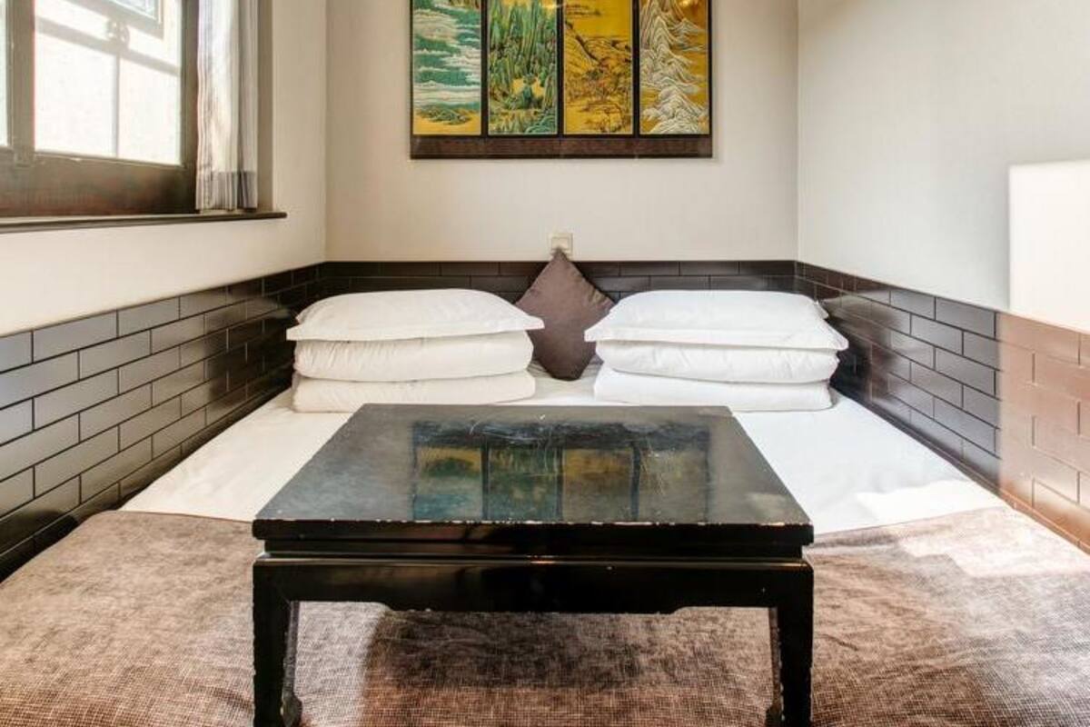 Une pièce comprenant un lit, des oreillers, une petite table et une œuvre d’art accrochée au mur.