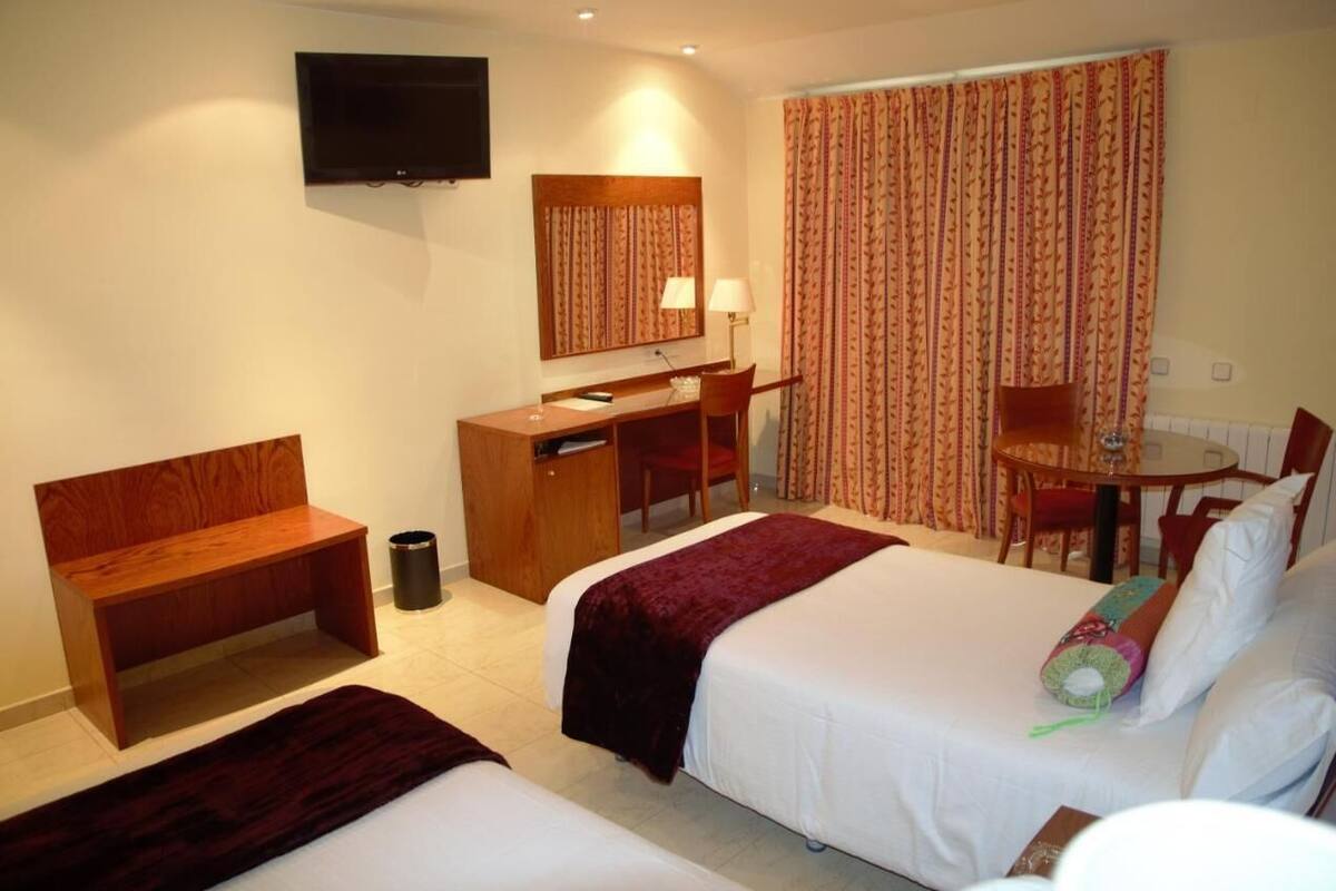 A hotel room with two beds, a desk, a chair, a TV, and a window with curtains.