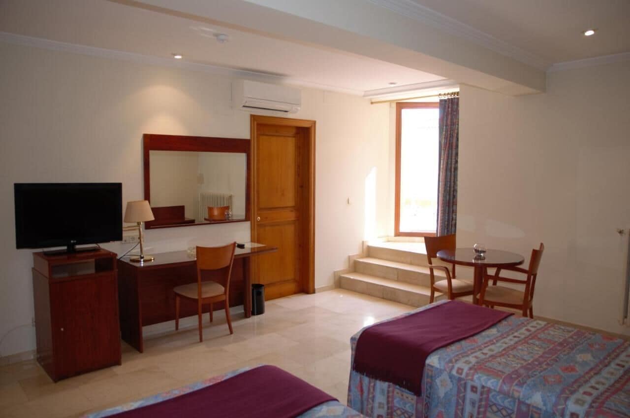 A hotel room with a bed, a desk with a chair, a television, and a window with curtains.
