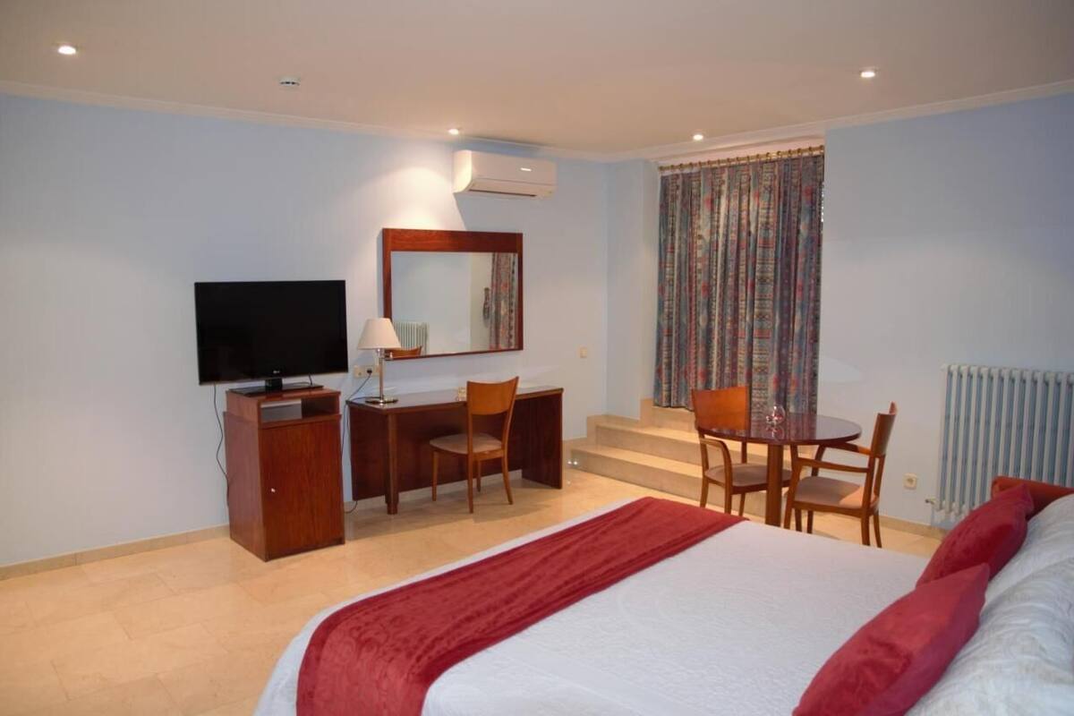 A hotel room with a bed, a desk with a chair, a television, and a window with curtains.