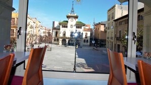 A view from a window with a table and chairs, overlooking a plaza with a clock tower and buildings. - Hotel Suis (Sant Celoni)