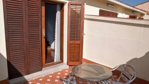 A small outdoor area with a round table and two chairs, a wooden door, and a window with shutters. - Hotel Suis (Sant Celoni)