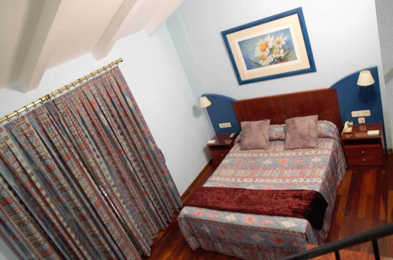 A bedroom with a bed, curtains, a framed picture, and bedside lamps.