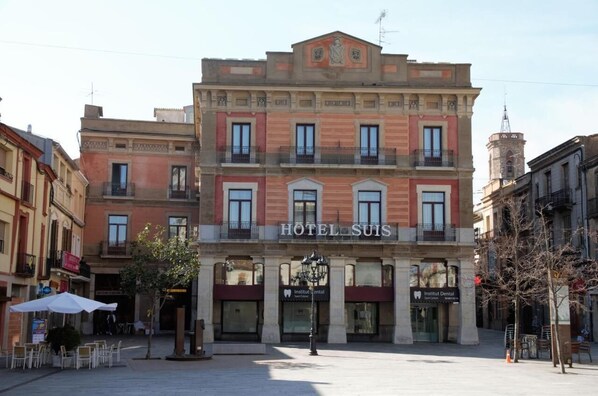 A hotel with a classic facade, multiple windows, and a sign that reads "HOTEL SUIS."