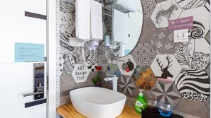 A bathroom with a white sink, a mirror, and a wall decorated with various animal and geometric patterns. There are towels hanging on a rack, a soap dispenser, and a bottle of hand soap on the counter. - Floral Hotel Jiu Qi Yin Ju Dunhuang (Jiuquan)
