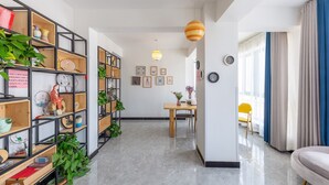 A modern living room with a wooden bookshelf, a dining area with a table and chairs, and a bright pendant light. - Floral Hotel Jiu Qi Yin Ju Dunhuang (Jiuquan)