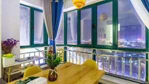 A room with a large window overlooking a cityscape, a wooden table, and a vase with flowers. - Floral Hotel Jiu Qi Yin Ju Dunhuang (Jiuquan)