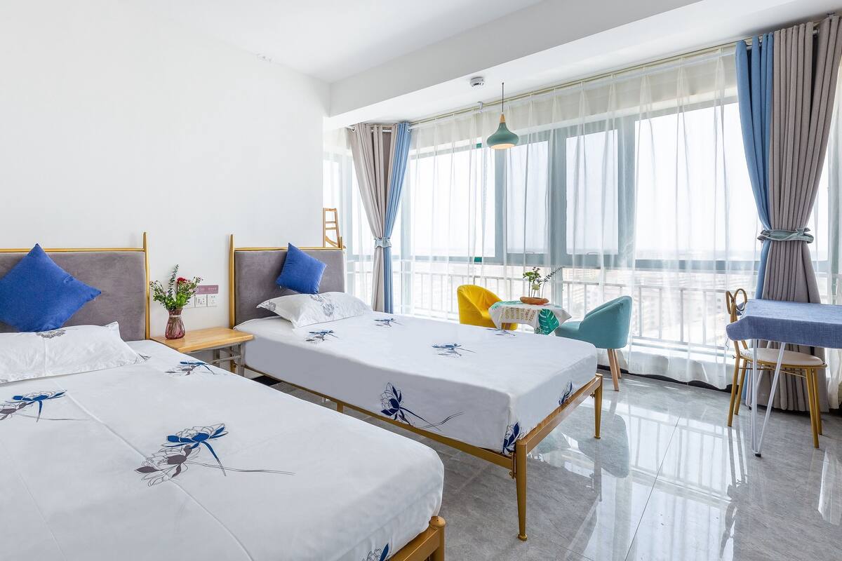 Ein Hotelzimmer mit zwei Betten, einem kleinen Tisch, einem Stuhl und einem Balkon mit Vorhängen.