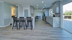 A spacious kitchen with a central island, bar stools, and a view through large sliding glass doors.