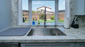 A kitchen with a sink, a window, and a view of a house and yard.