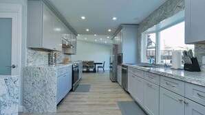 A modern kitchen with marble countertops, wooden flooring, and a view through the window.