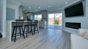 A spacious living area with a kitchen, a large TV mounted on the wall, and a fireplace.