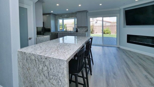 A modern kitchen with a marble island, bar stools, and a large TV mounted on the wall.